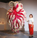 Person standing next to a large, intricate costume with red and white design