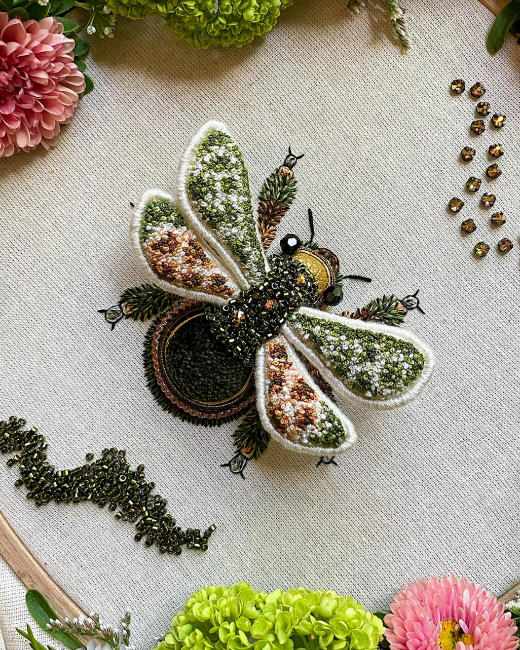 Embroidered bee design on fabric with flowers and beads around