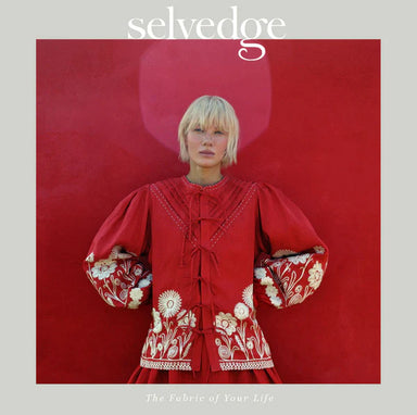 Person wearing a red embroidered dress with floral patterns on a red background, featuring the brand 'selvedge'.