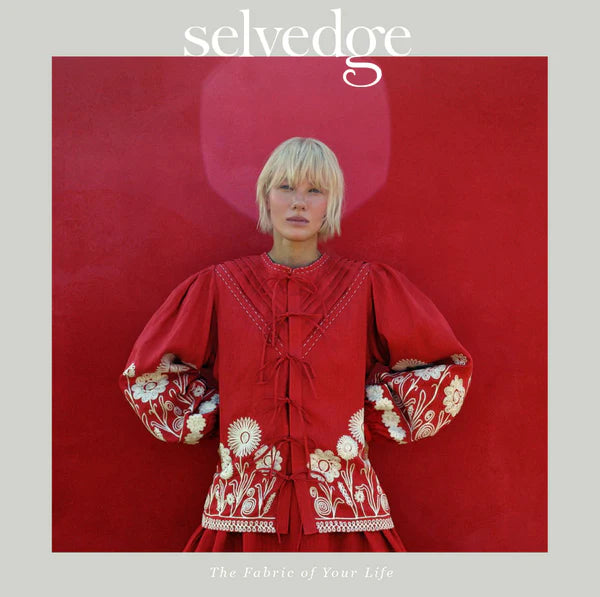 Person wearing a red embroidered dress with floral patterns on a red background, featuring the brand 'selvedge'.