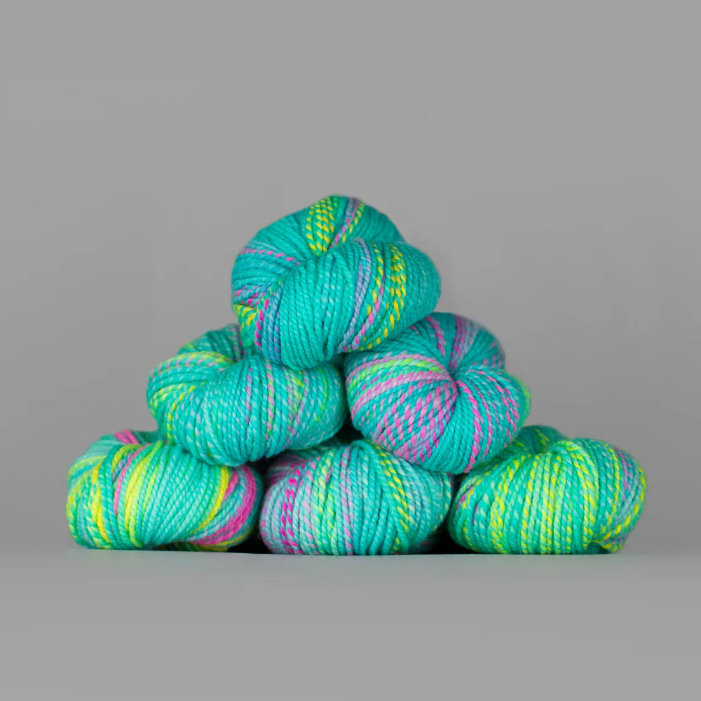 Turquoise yarn with green and pink stripes stacked on a gray background
