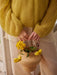 Person wearing a yellow sweater holding a woven basket with yellow flowers.