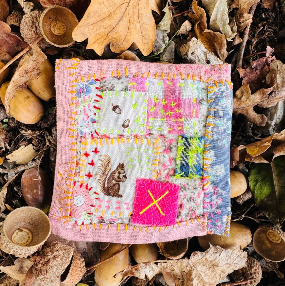Small patchwork square with a pink border on a bed of leaves and acorns
