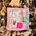 Small patchwork square with a pink border on a bed of leaves and acorns