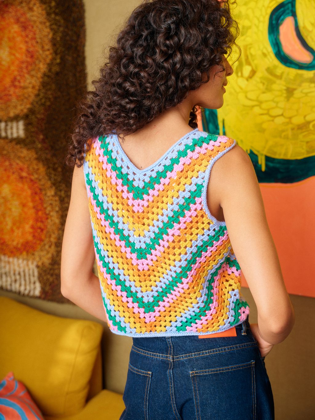 Person wearing a colorful crochet tank top in a room with vibrant decor.