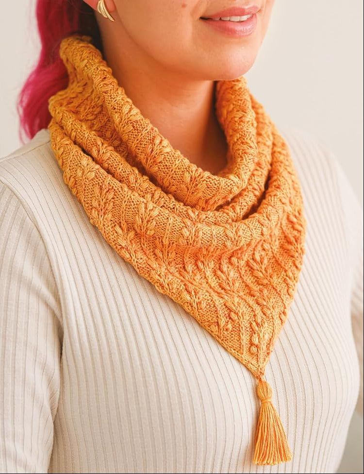Knitted orange cowl worn by a person with pink hair, alongside knitting pattern text.