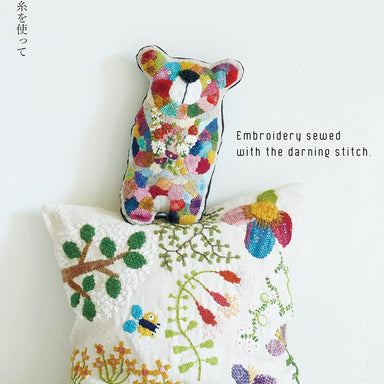 Embroidered pillow with colorful bear design and text about darning stitch embroidery.