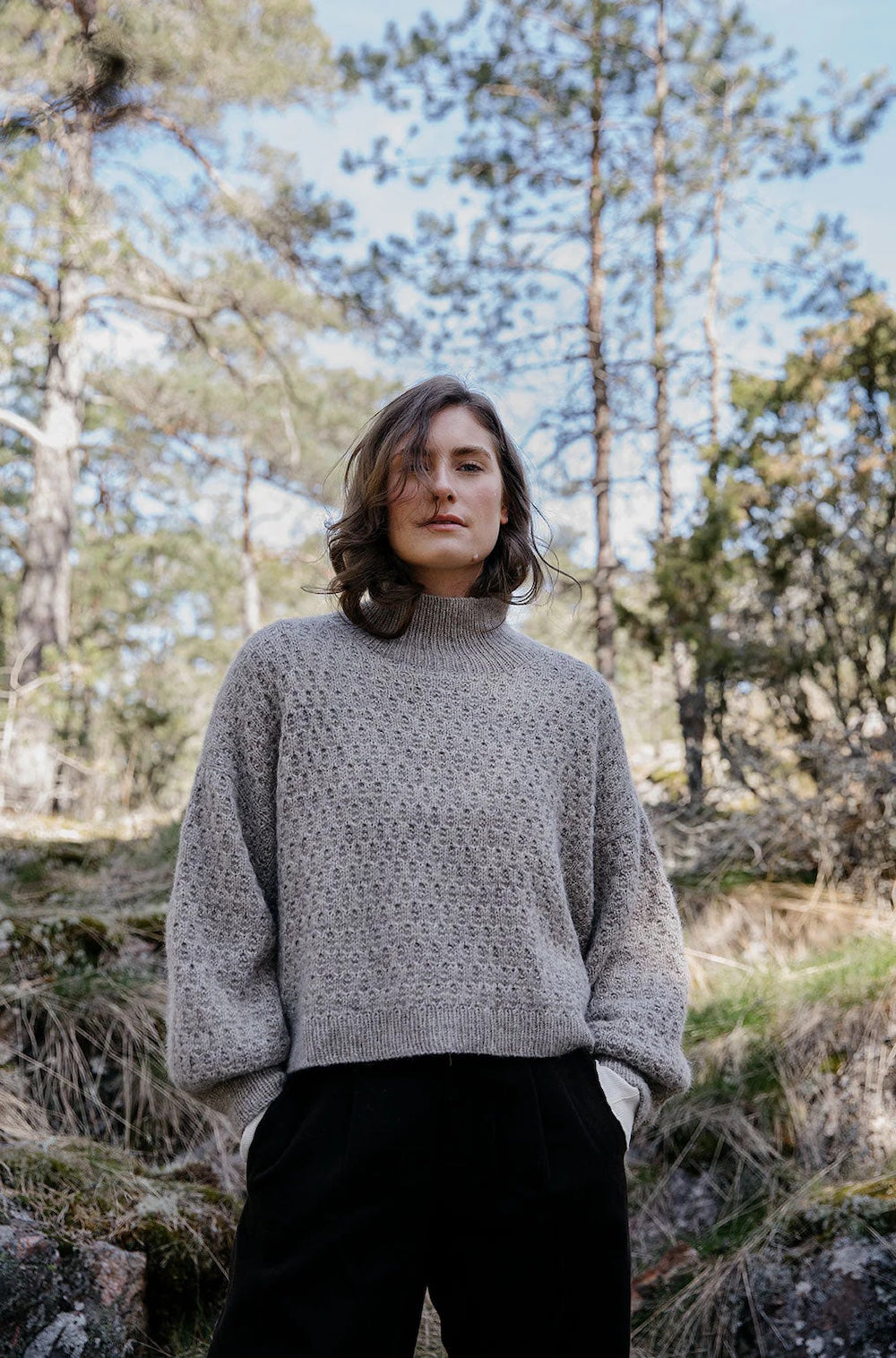 Person wearing a gray sweater in a forest setting