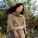 Woman wearing a beige poncho standing outdoors with trees in the background
