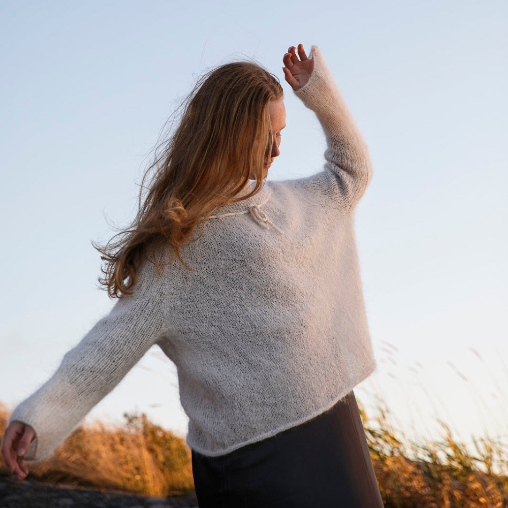 Woman in a light sweater standing outdoors with a clear sky