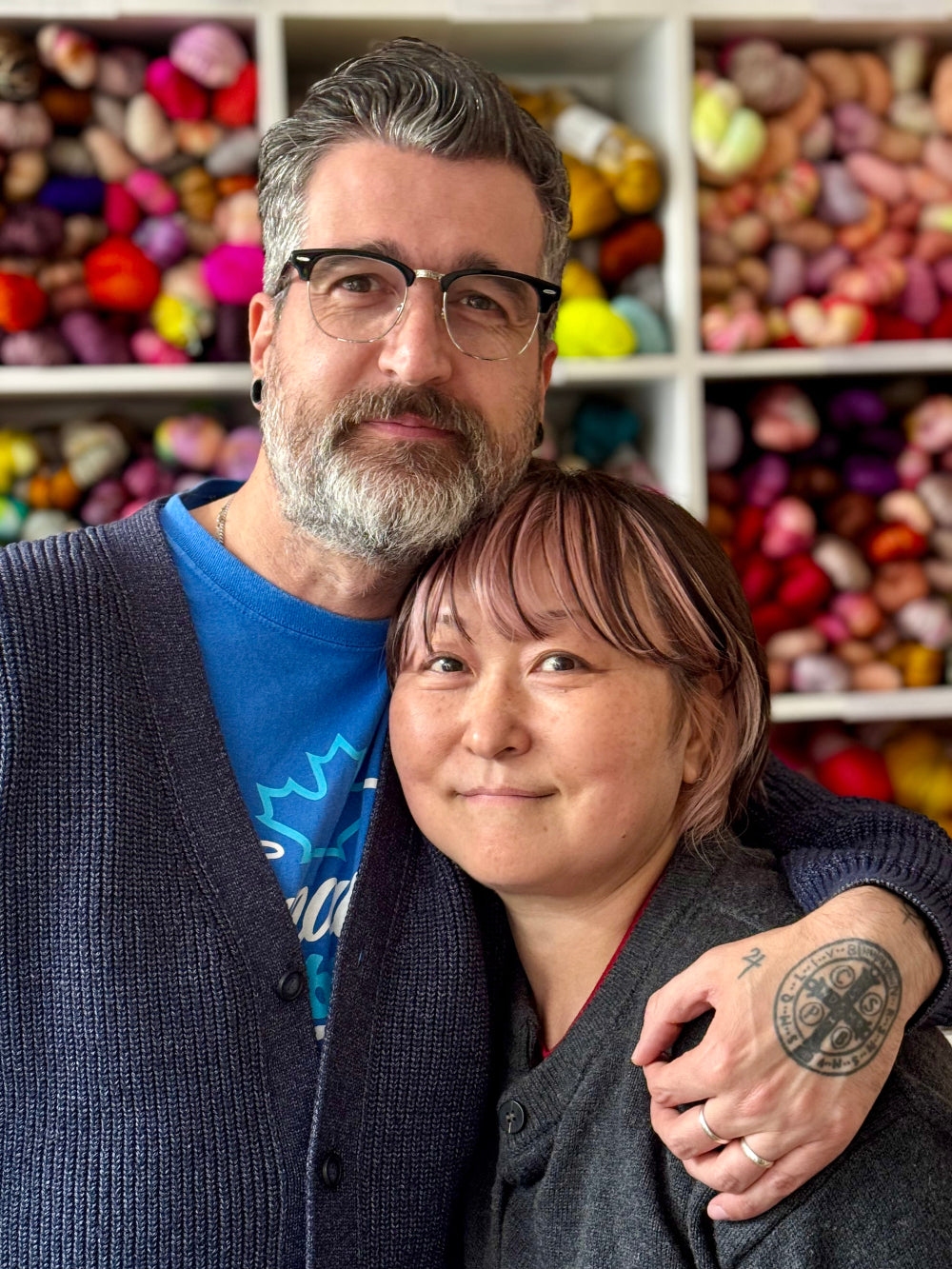 Two people standing together with a colorful yarn background
