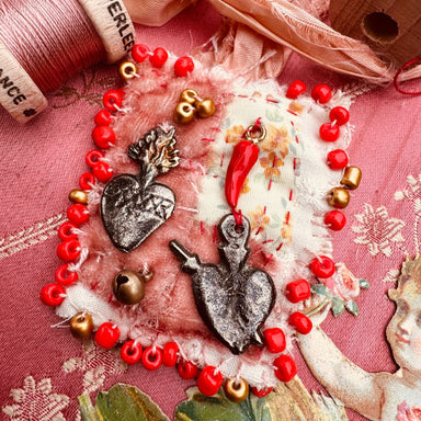 Heart-shaped charm bracelet with red beads on a pink fabric background