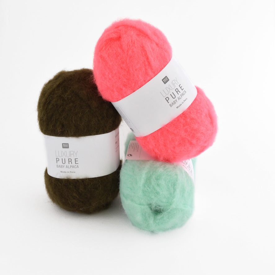 Three balls of yarn in pink, brown, and green on a white background