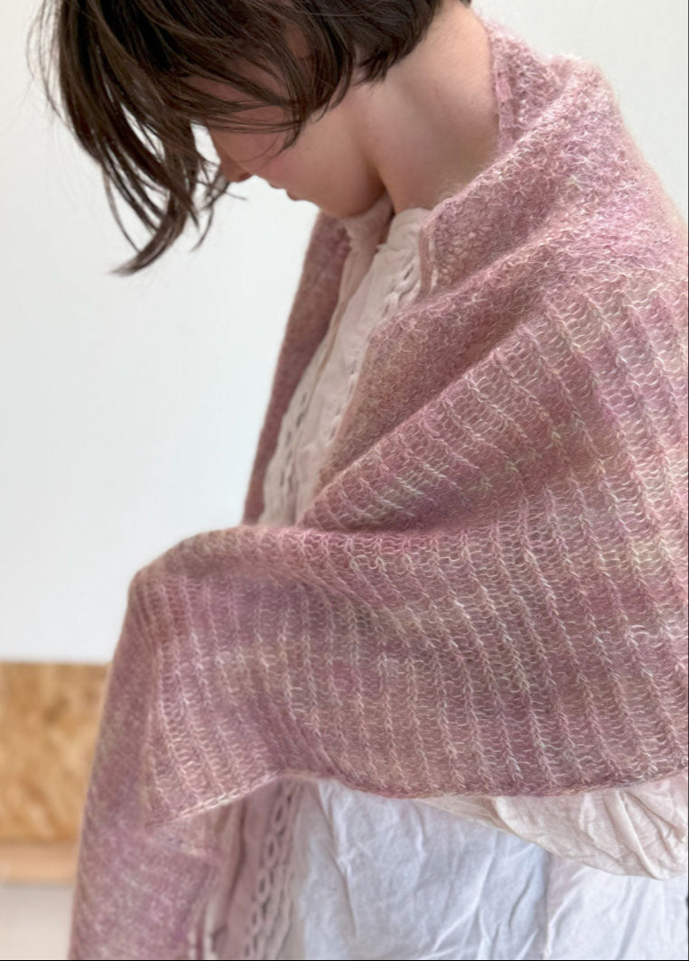 Person wearing a pink knitted shawl over a white garment against a light background