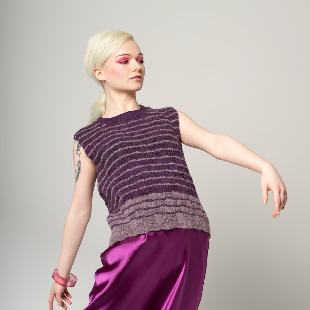 Person wearing a sleeveless purple top and skirt with blue jeans on a gray background