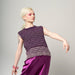 Person wearing a sleeveless purple top and skirt with blue jeans on a gray background