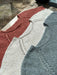 Three knitted sweaters in red, white, and gray on a wooden surface.