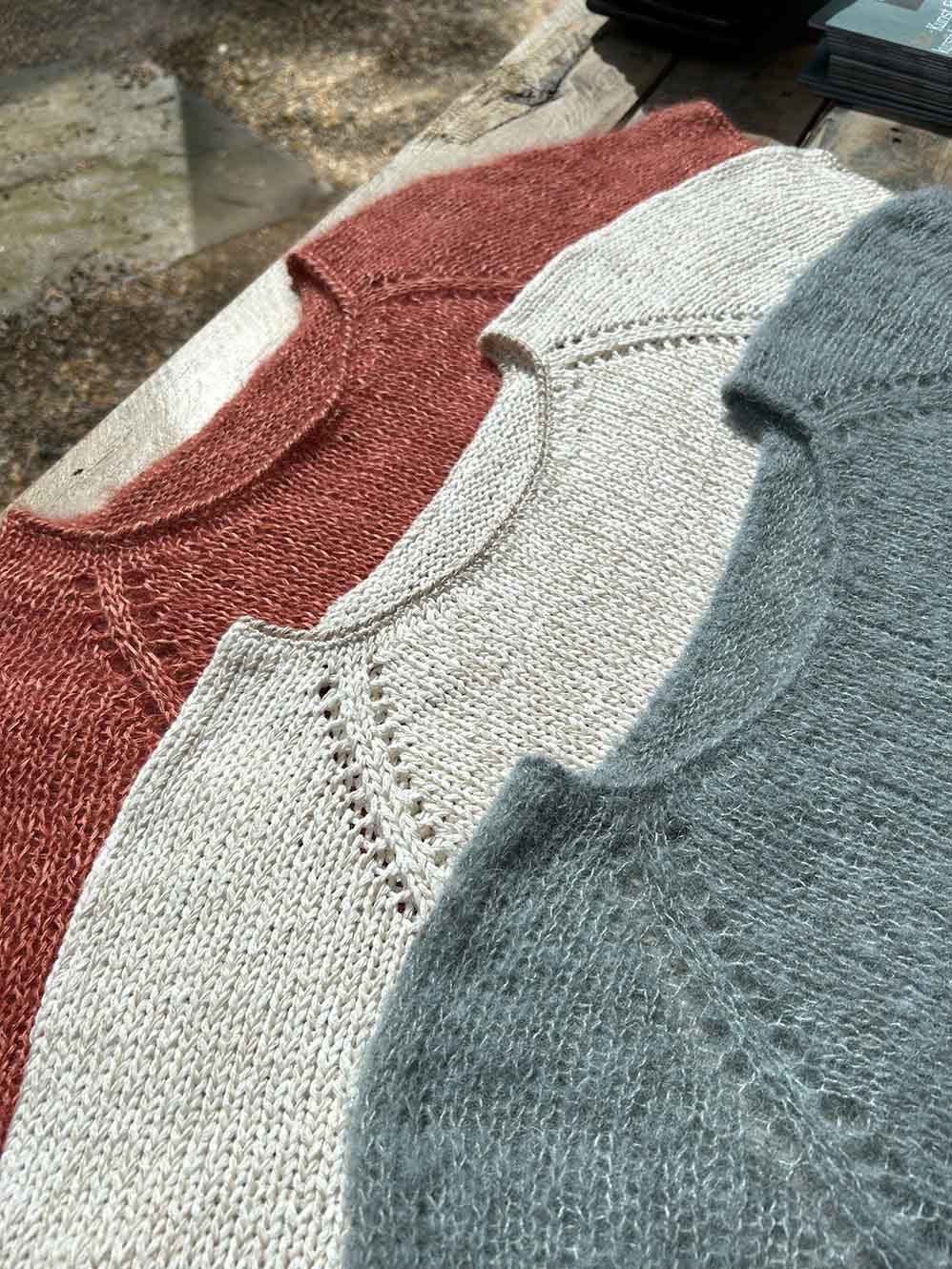Three knitted sweaters in red, white, and gray on a wooden surface.
