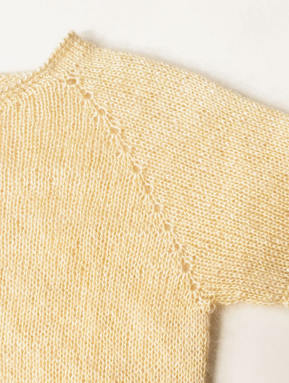 Close-up of a light beige or cream-colored knit garment, showing the fine knit texture and a decorative pointed lace or eyelet stitch detail along the neckline.