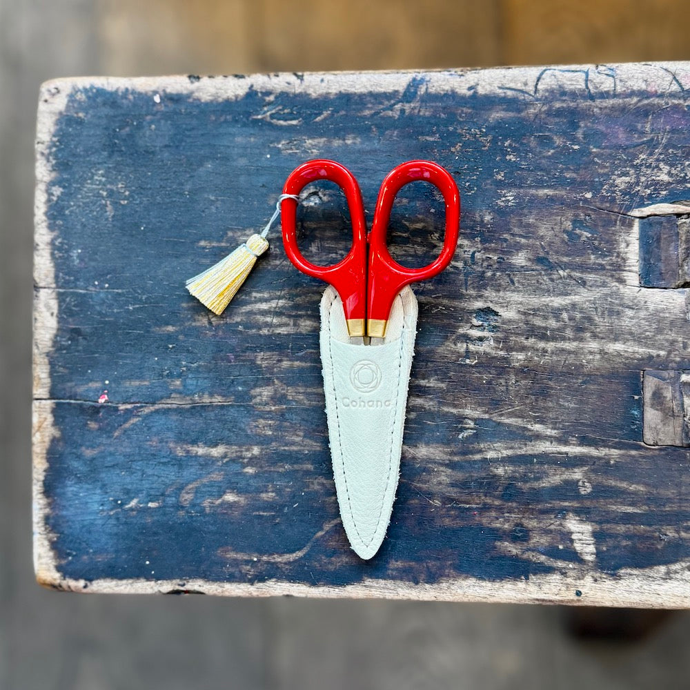 Red scissors with a white sheath on a wooden surface
