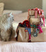 Cat sitting next to a suitcase with colorful ribbons and decorations on a bed.