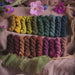 Colorful yarn skeins arranged in a gradient on a textured surface with flowers.
