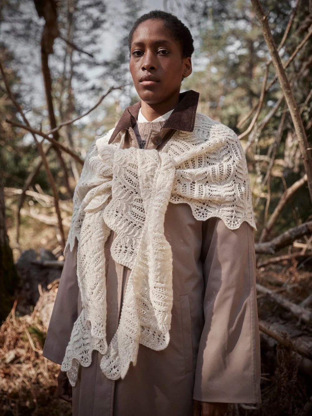 Person wearing a beige coat with a white lace shawl in a forest setting
