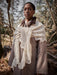 Person wearing a beige coat with a white lace shawl in a forest setting