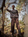 Person wearing a patterned sweater and brown pants standing in a forest.