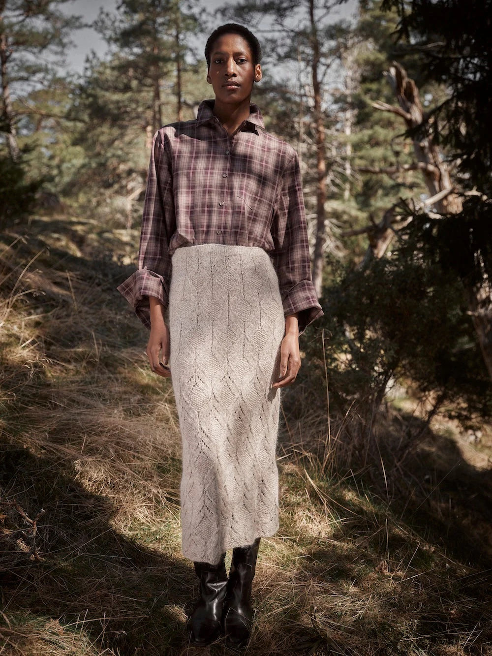 Person wearing a plaid shirt and knitted skirt standing in a forest