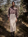 Person wearing a plaid shirt and knitted skirt standing in a forest