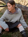 Woman sitting outdoors wearing a cable knit sweater and dark pants.