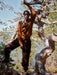 Person in a brown sweater and pants standing on a log in a forest setting