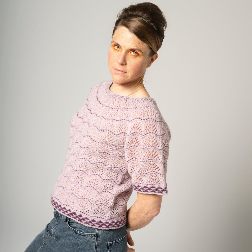 Person wearing a pink knit sweater and blue jeans on a gray background