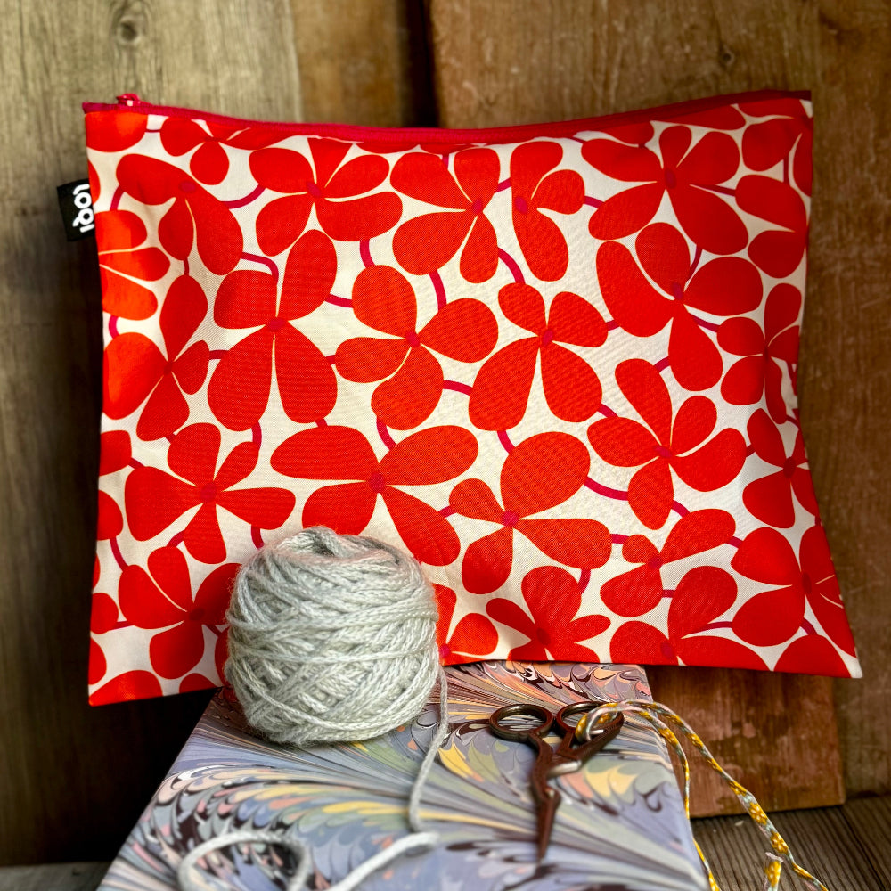 Red floral-patterned pouch with a ball of yarn and scissors on a wooden surface