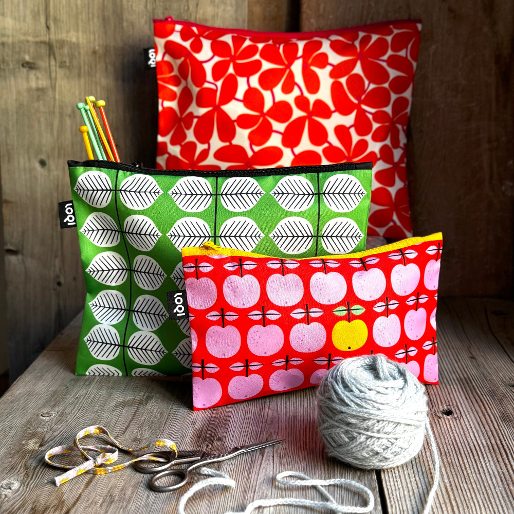 Three patterned pouches on a wooden surface with yarn and scissors.