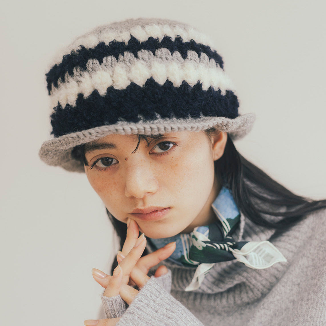 Person wearing a striped knit hat and gray sweater with a white background