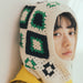 Person wearing a crocheted balaclava with geometric patterns on a plain background