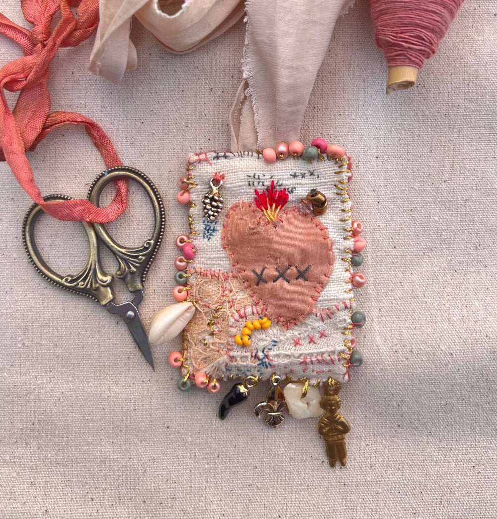 Handmade heart-shaped fabric ornament with decorative elements on a textured surface with scissors and thread.