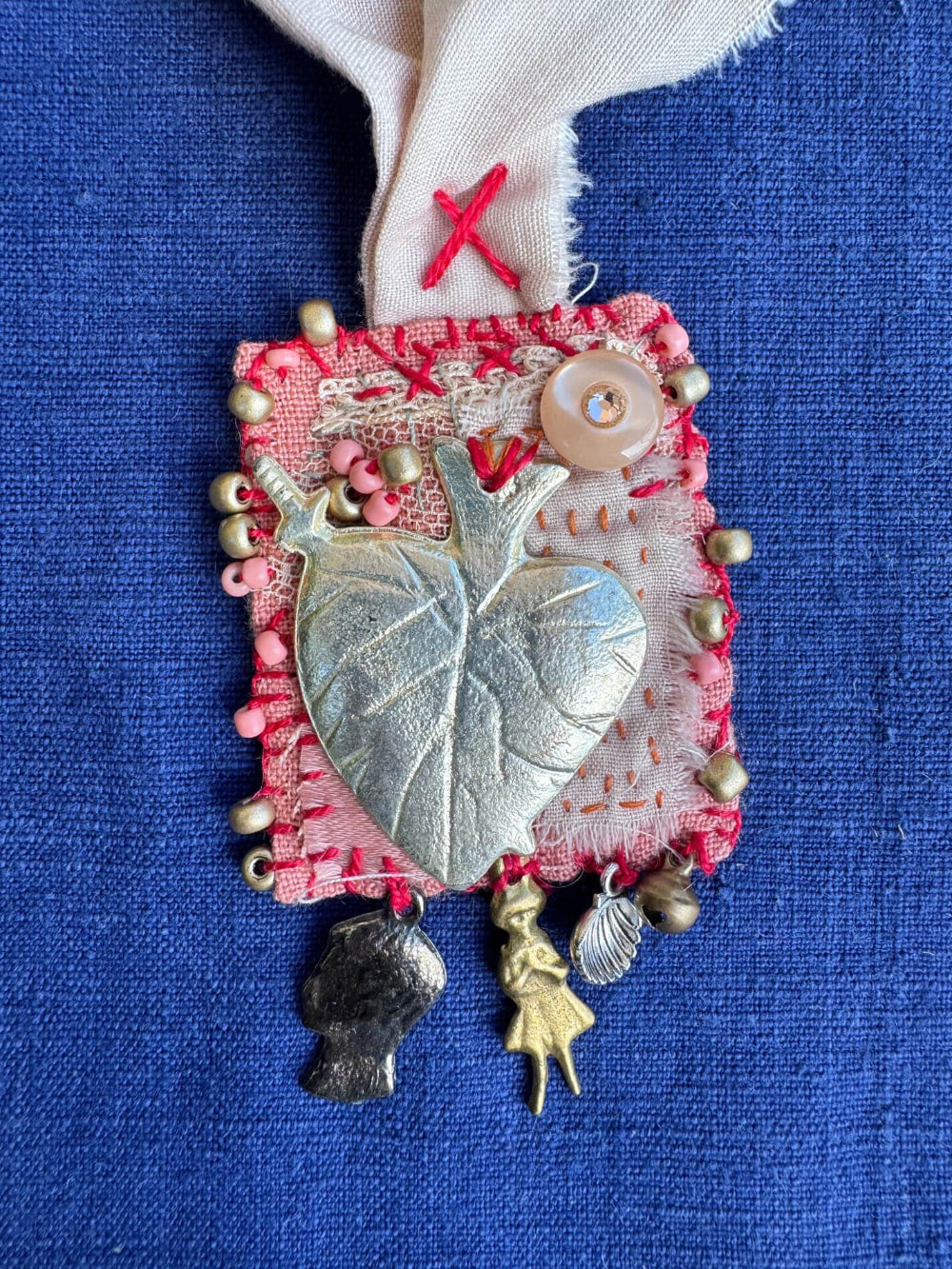 Decorative brooch with leaf design and various charms on a blue background