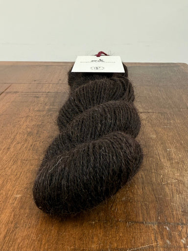 Three skeins of dark brown yarn on a wooden surface with a white background