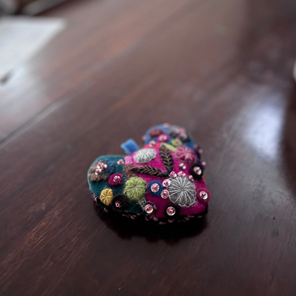 Decorative heart-shaped object with colorful embroidery on a wooden surface