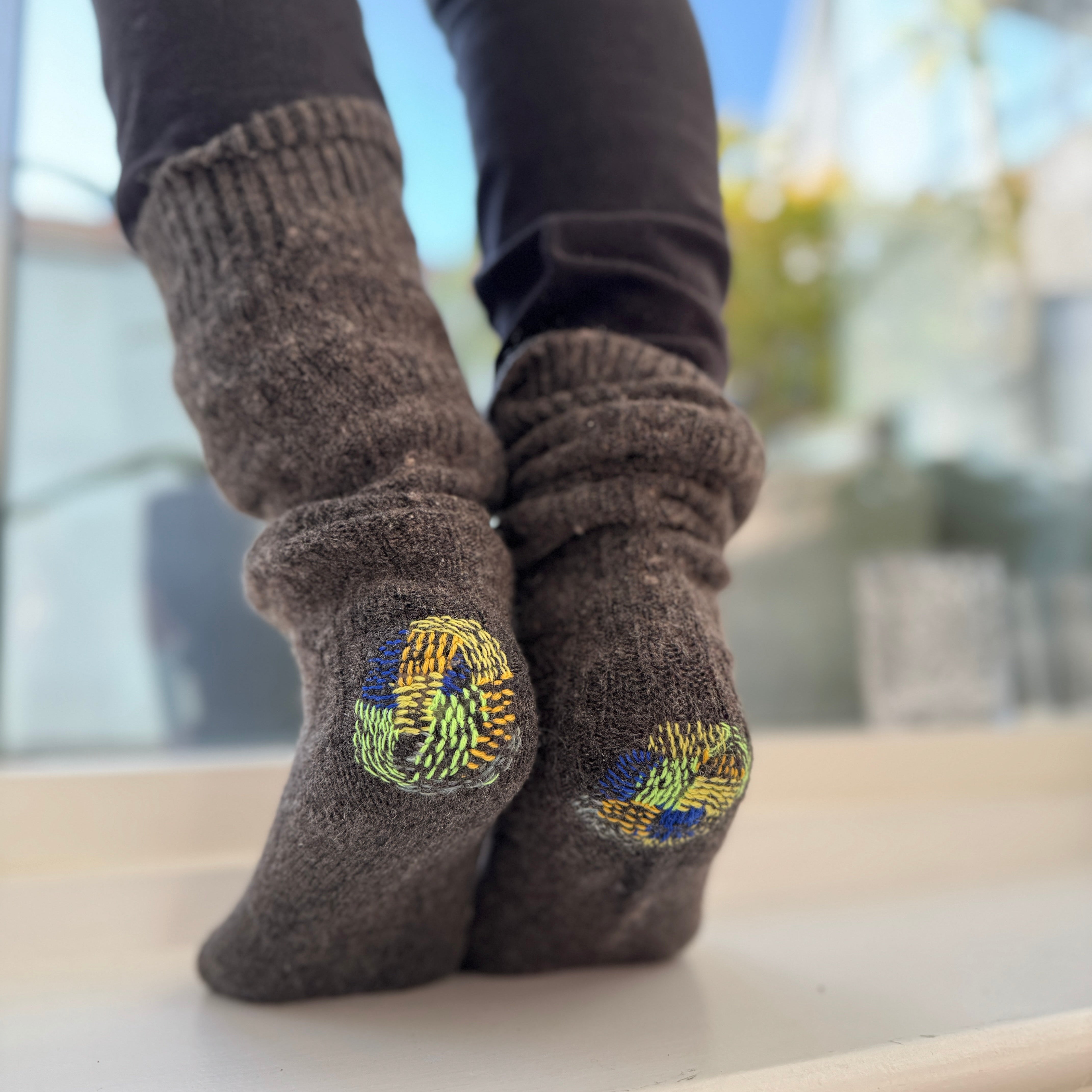 Brown socks with colorful designs worn by a person standing on a ledge.