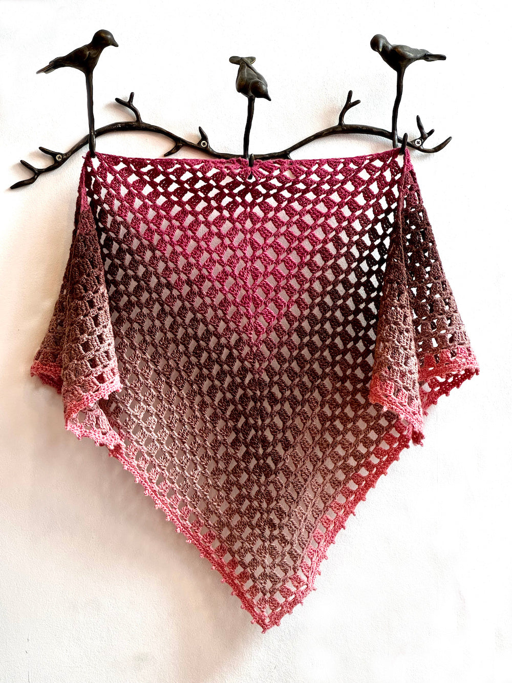 Knitted shawl with a gradient pattern on a white background with decorative birds on a branch.