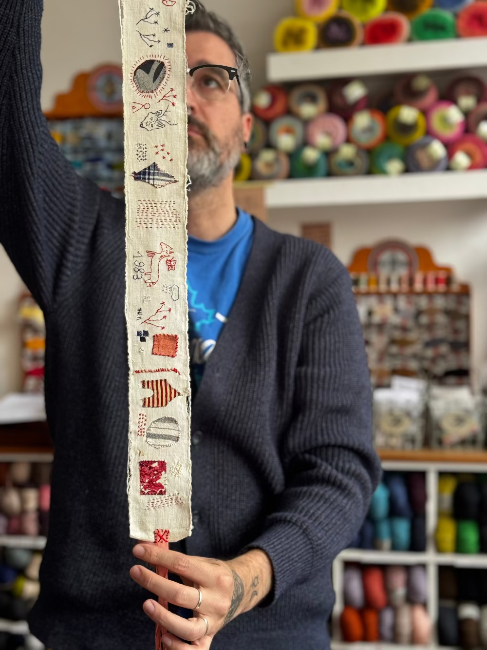 Man holding a decorative fabric strip with patterns in a yarn store.