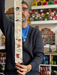 Man holding a decorative fabric strip with patterns in a yarn store.