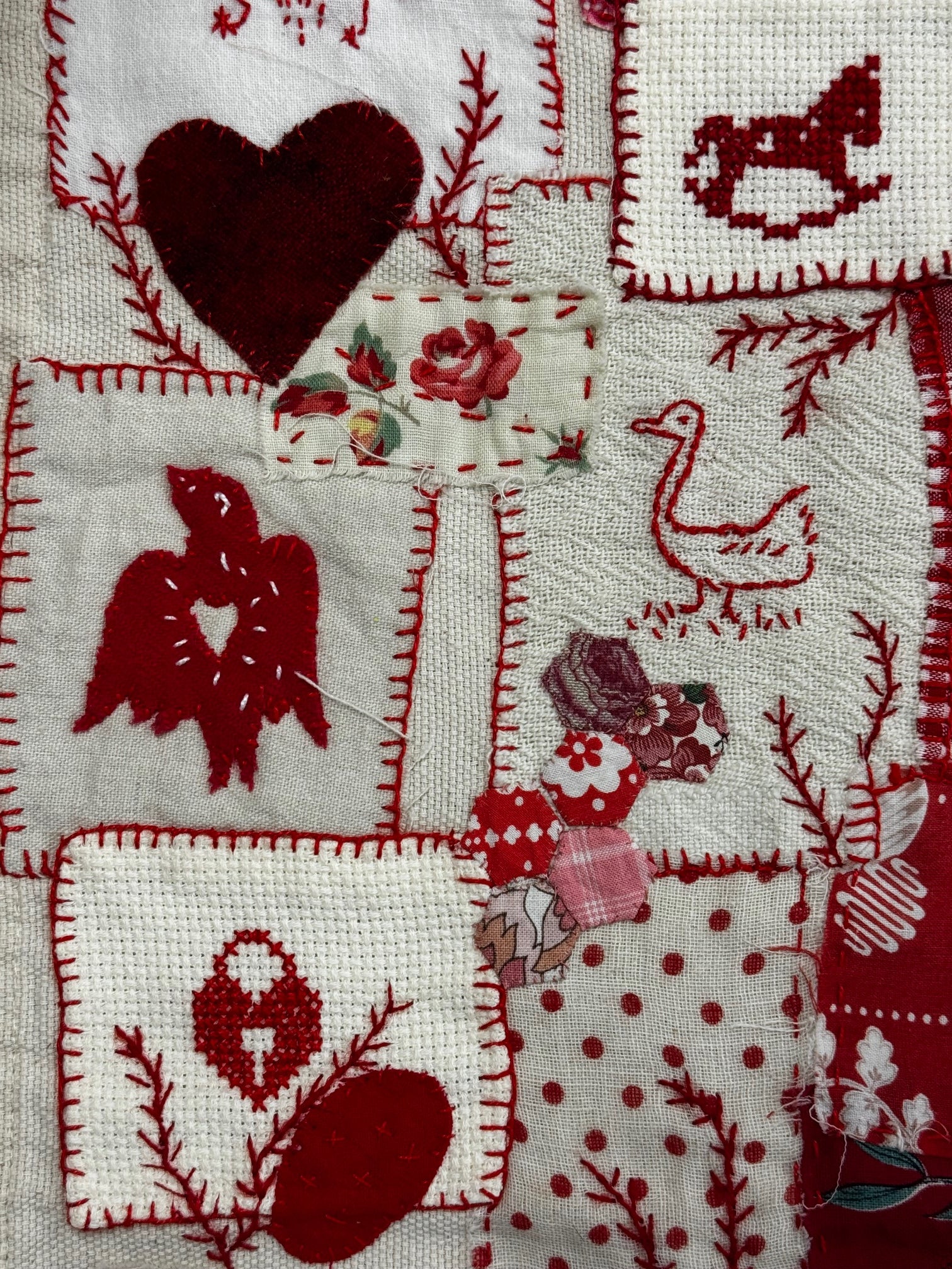 Embroidered fabric with red and white patterns including hearts, birds, and floral designs.