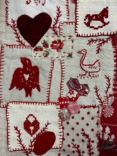 Embroidered fabric with red and white patterns including hearts, birds, and floral designs.