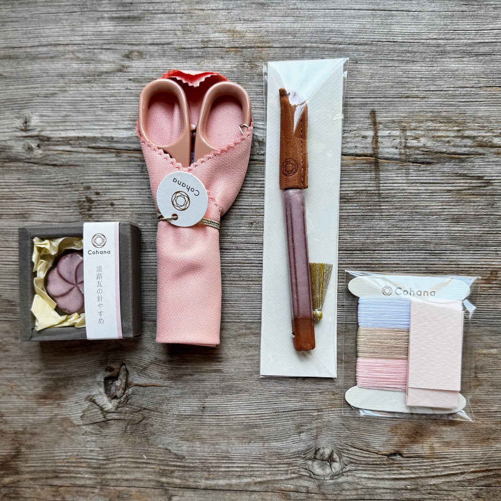 Set of pink scissors, knife, and thread on a wooden surface with Cohana branding.