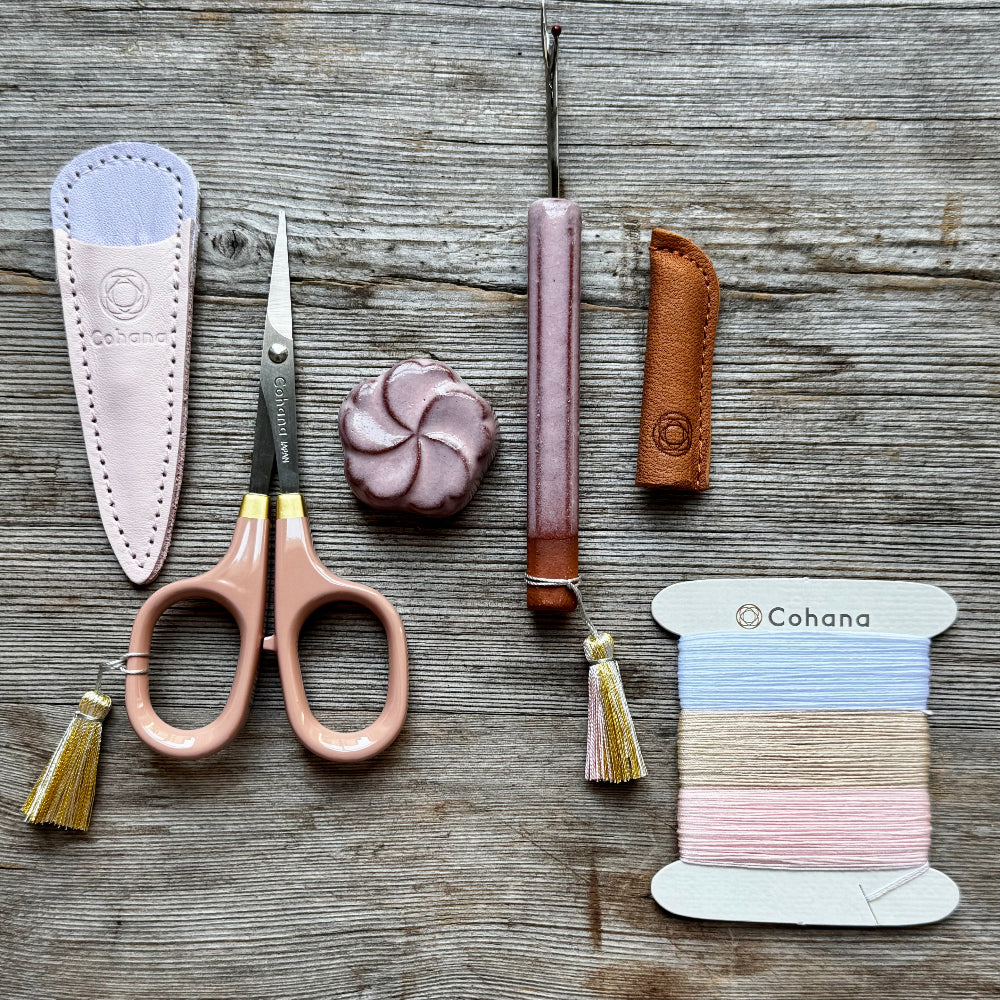 Scissors with sheath, spool of thread, and leather items on a wooden surface